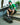 Person in Panathinaikos shirt and hat sitting on a skateboard with graffiti in the background