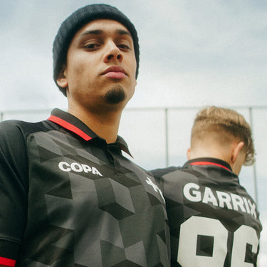 MARTIN GARRIX x COPA Football Shirt Black Lifestyle Shot featuring two models wearing the jersey in an urban football setting.