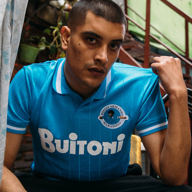 Model wearing the Maradona X COPA Napoli 1986-87 Retro Football Shirt, seated in an urban setting, showcasing its fit and style.