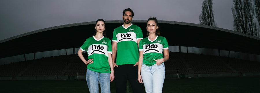 Three people wearing green St. Gallen shirts standing on a grassy field with a dark sky.