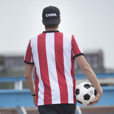 Football player wearing a red and white striped jersey and COPA trucker cap, holding a soccer ball