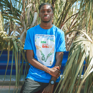 Model wearing the 2014 World Cup T-shirt, standing outdoors, showcasing the poster-inspired football-themed design.