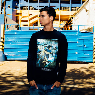 Model wearing the Maradona x COPA Bombonera Sweater in front of blue stadium seats