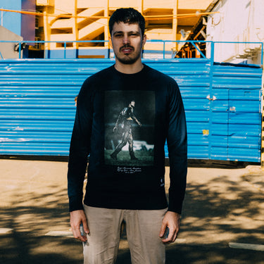 Model wearing the Maradona x COPA Muddy Pitch Sweater outdoors in front of blue stadium seating