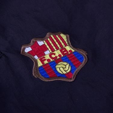 Close-up of embroidered FC Barcelona crest on navy fabric, showing detailed stitching in red, yellow, blue, and brown.